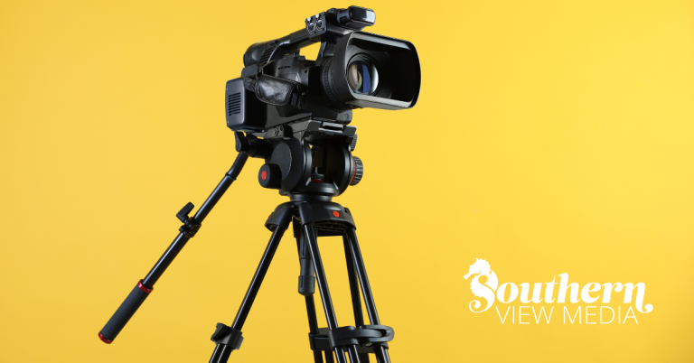 A professional black digital video production camera mounted on a sturdy tripod against a solid, bright vibrant yellow background.